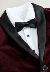 Hvid skjorte under en burgundy fløjlsjakke med sorte satin reverser og en sort butterfly.