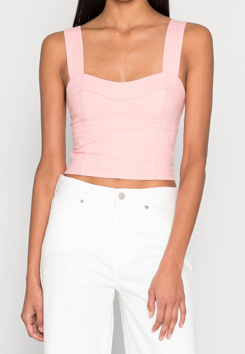 Haut court rose clair avec encolure carrée structurée, larges bretelles et coutures discrètes. Associé à un pantalon blanc taille haute.