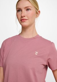 Lyserød bomulds-t-shirt med rund halsudskæring og korte ærmer, med et lille cremefarvet chevron-logo på venstre brystområde.