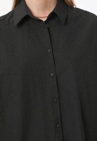 Black button-up shirt with a classic collar, smooth texture, and six front buttons. Simple design without patterns or embellishments.
