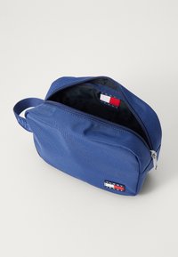 Borsa a spalla in nylon blu con apertura con zip, dotata di etichetta Tommy Jeans e una robusta tracolla in tessuto. Fodera interna di colore scuro.