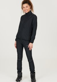 Sort udendørsjakke og bukser sæt lavet af letvægtsmateriale. Har en lynlåsåbning fortil, høj krave og reflekterende detaljer på bukserne.