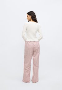 Bijela bluza s dugim rukavima uparena s visokim strukom prugastih hlača u ružičastoj i bijeloj boji. Tkanine izgledaju mekano; hlače imaju široke manžete.