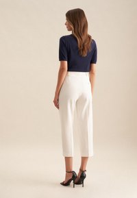 Marineblaues Kurzarmoberteil kombiniert mit hochgeschnittenen weißen Culottes. Das Modell trägt schwarze High Heels. Glatte Texturen und taillierte Passform.