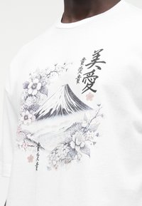 Weißes Baumwoll-T-Shirt mit einem grafischen Druck von Mount Fuji, Blumendesigns in Grautönen und schwarzem Text mit japanischen Schriftzeichen.