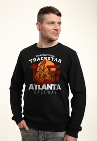 Svart sweatshirt med en grafisk design av en motorcyklist, orange cirkelbakgrund och vit text som säger "International Trackstar Atlanta Raceway."