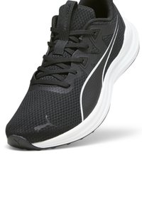 Scarpa sportiva nera con tomaia in rete, intersuola bianca e suola testurizzata; presenta lacci e un logo sul lato.