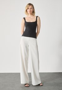 Top de tirantes negro con escote cuadrado, combinado con pantalones anchos blancos. Textura suave y diseño sencillo. Sandalias negras completan el look.