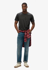 Grijze katoenen T-shirt met een borstzak, gecombineerd met lichtblauwe spijkerbroeken. Een rood en zwart geruit overhemd geknoopt om de taille, witte sneakers.