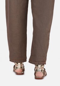 Bruine wijde broek met rafelige zoom, gecombineerd met metallic gouden en bruine sandalen met ronde hardware details.