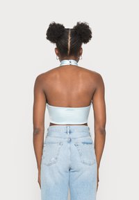 Top cropped halter em satin azul claro, com fecho nas costas, ombros expostos e design justo, combinado com jeans azul claro de cintura alta.