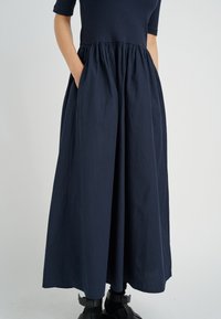 Navyblaue lange Rock mit gerafftem Bund, aus leichtem Stoff gefertigt. Verfügt über seitliche Taschen und eine glatte Textur.