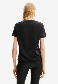 Camiseta negra de manga corta hecha de algodón, con un corte relajado y cuello redondo. La parte posterior es lisa, sin patrones ni acentos.