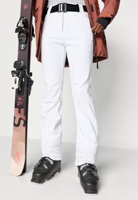 Fehér, egyenes szabású sínadrág cipzáras zsebbel és megerősített varratokkal. Fekete síbakancsok és snowboard kíséri.