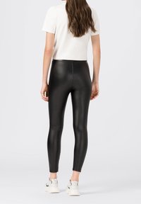 Svarta fusklädersleggings med en sömlös midja, smal passform och ankellängd, kombinerat med en vit kortärmad topp och vita sneakers.