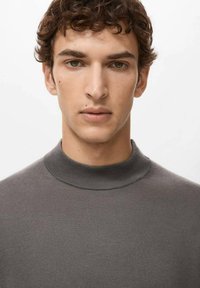 Szary dziany sweter z wysokim kołnierzem, dopasowanym krojem i delikatną fakturą, prezentowany na modelce na białym tle.