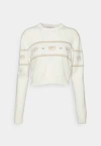 Pull blanc court à manches longues, col rond, avec des motifs beiges en forme d'œil et d'étoile sur la poitrine et le haut des bras.