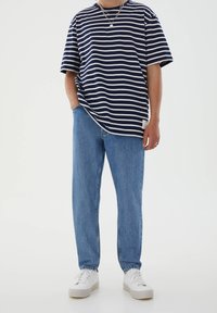 Marinblå och vit randig t-shirt med korta ärmar som är kombinerad med ljusblå raka jeans och vita sneakers, med en mjuk bomullstextur.