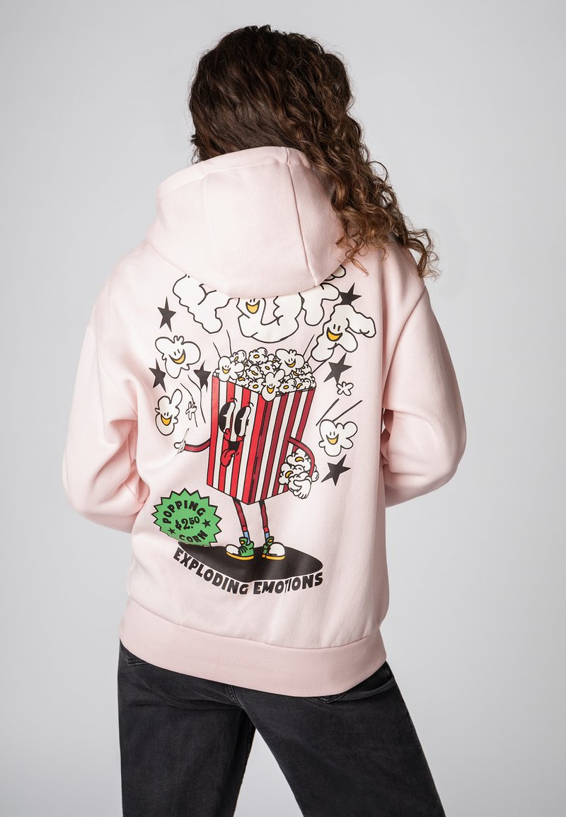 Roze hoodie met een cartoon popcorn personage dat in een gestreepte verpakking zit, omringd door lachende popcorn en sterren.