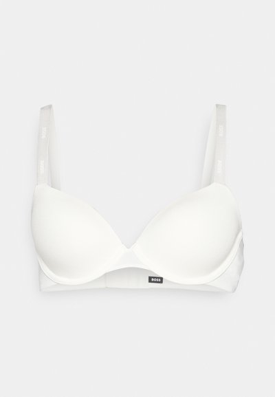 Soutien-gorge blanc matelassé avec des bretelles ajustables, présentant une texture de tissu lisse et un petit logo noir sur la bande. Design simple et minimaliste.