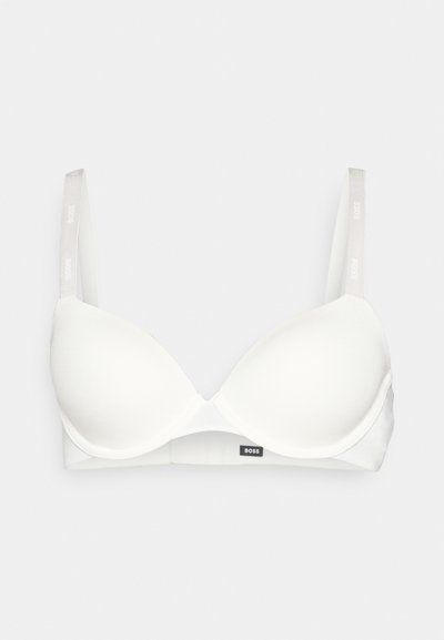 Soutien-gorge blanc matelassé avec des bretelles ajustables, présentant une texture de tissu lisse et un petit logo noir sur la bande. Design simple et minimaliste.