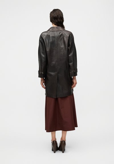 Μακρύ μαύρο δερμάτινο παλτό με χαλαρή εφαρμογή, γιακά που γυρίζει προς τα κάτω και μανσέτες με κουμπιά, με λεία υφή και μέτριο μήκος.