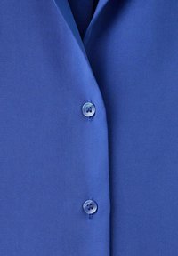 Gros plan d'un vêtement bleu avec deux boutons bleus assortis attachés le long d'une couture centrale.