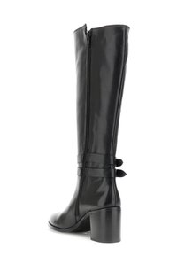 Bota alta de cuero negro con tacón cuadrado, cremallera lateral y correas decorativas alrededor del tobillo sobre un fondo blanco.