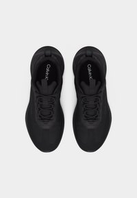 Paire de baskets noires Calvin Klein avec lacets, vues de dessus sur un fond blanc.