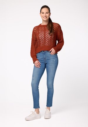 Burnt orange knitted sweater with a chevron pattern, paired with light blue ripped skinny jeans and white sneakers.