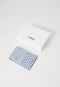 Hellblauer Leder-Kartenhalter mit vier Fächern, goldenen Hardware-Details und einem Reißverschlussfach, neben einer weißen Geschenkschachtel mit Branding platziert.