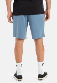 Lichtblauwe katoenen shorts met een elastische tailleband, zijzakken en een achterzak. Gecombineerd met zwarte schoenen en witte sokken.