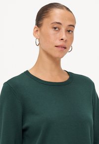 Grønn strikket genser med rund hals, med en jevn tekstur og subtile ribbede detaljer ved halsen og mansjettene.