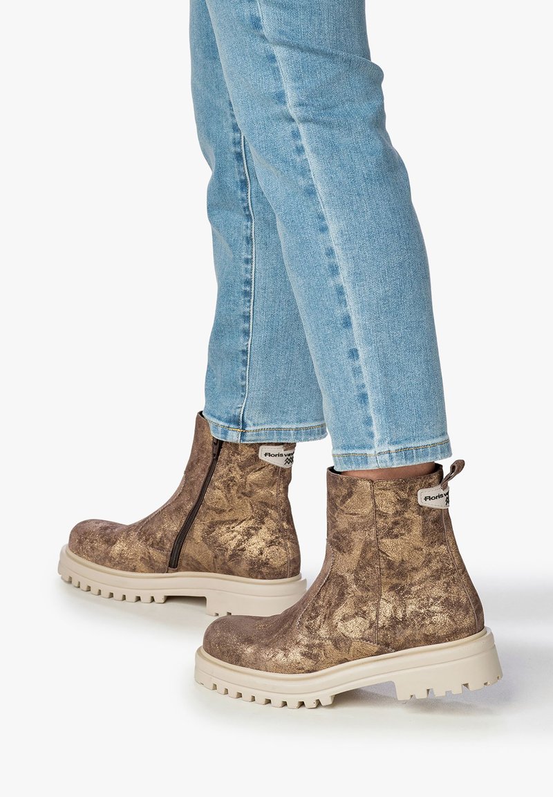 Bottines métalliques brunes avec une finition texturée, fermeture éclair sur le côté et semelle en caoutchouc clair. Portées avec un jean bleu, montrant les jambes inférieures.
