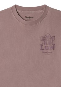 Šviesiai mauve spalvos medvilnės marškinėliai su apvaliu iškirpimu ir spausdinta grafika, vaizduojančia riedlentę su užrašu "LDN" ir prekės ženklu purpuro spalva.