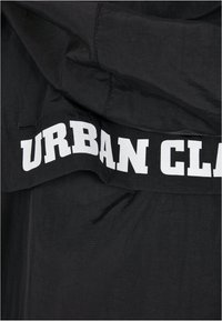 Un tissu noir à texture lisse présente un texte imprimé blanc en lettres majuscules "URBAN CLASS" le long du bord inférieur.