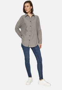 Camicia a righe bianche e nere con colletto, maniche lunghe e vestibilità rilassata, abbinata a jeans skinny blu e sneaker bianche.