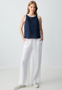Top senza maniche blu navy con rifiniture bianche; pantaloni ampi in lino bianco; scarpe casual; texture liscia, vestibilità rilassata.