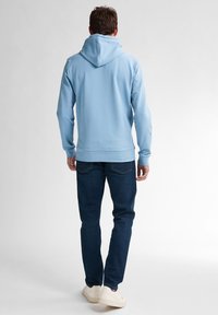 Sudadera de color azul claro con un bolsillo tipo canguro, puños acanalados y dobladillo. Combinada con jeans oscuros y zapatos blancos. Textura de tela suave.