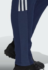 Navy blue athletic pants with white stripes, featuring a side pocket, soft fabric, and a tapered design for a snug fit.