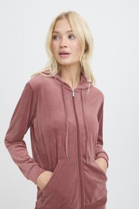 Felpa con zip in velour rosa, dotata di cappuccio, tasche frontali e stringhe regolabili. Texture morbida e polsini fitted. Design semplice, senza motivi o accenti.