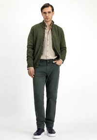Green knit cardigan with textured fabric and buttons, paired with a beige button-up shirt and dark green pants. Features black sneakers.