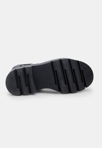 Suela de zapato de goma negra con un patrón texturizado, que presenta ranuras y crestas horizontales para un agarre y estabilidad óptimos. Forma plana y redondeada.