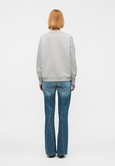 Γκρι φούτερ με στρογγυλή λαιμόκοψη και ριμπ μανσέτες, συνδυασμένο με ανοιχτό μπλε τζιν καμπάνα, με σχισμή στη ραφή στο τελείωμα.