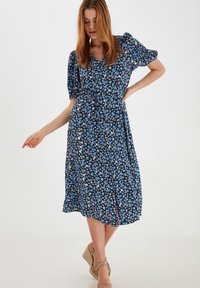 Blaues Blumenmusterkleid mit Puffärmeln, V-Ausschnitt, tailliertem Schnitt und knielangem Rock. Hergestellt aus leichtem Stoff, mit einem dunklen Hintergrund.