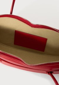 Intérieur d'un sac à main en cuir rouge avec une doublure en beige texturée, fermeture zippée et étiquette embossée. Présente des bords nets et un design minimaliste.