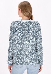 Huvtröja i teal med vitt leopardmönster, med långa ärmar och en något avslappnad passform, tillverkad av lättviktig tyg.