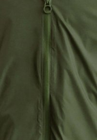 Giacca verde oliva con cerniera a tutta lunghezza, caratterizzata da una texture liscia e opaca con una lucentezza sottile. Tiretto della cerniera visibile nella parte superiore.