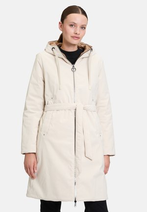 Manteau long beige imperméable avec capuche, fermeture éclair, ceinture ajustable à nouer et poches latérales. Texture douce avec une finition lisse.