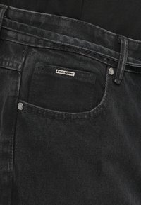 Črne denim hlače z običajno zasnovo žepov, kovinsko gumbom in teksturirano tkanino z v woven vzorcem. Oznaka "PEGADOD" na hrbtni strani.